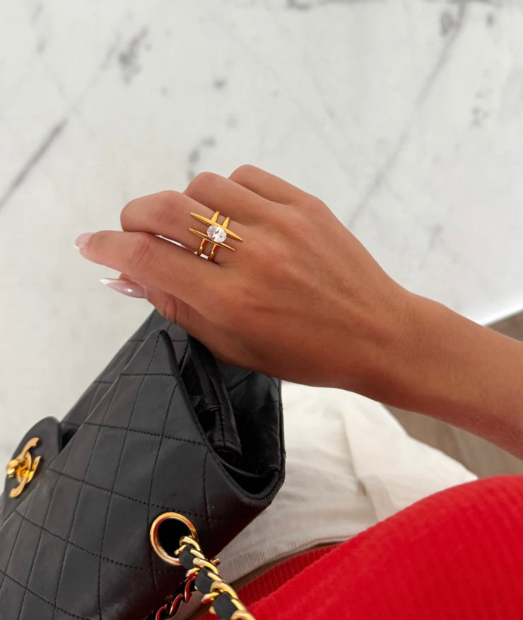 bold gold-tone ring features a striking geometric silhouette, flanked by sculpted bars and a radiant center stone