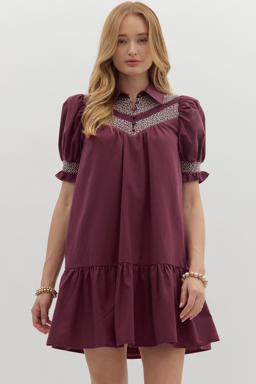 Woman wearing a berry-colored mini dress with puff sleeves, smocked yoke detail, collared neckline, and ruffled tiered hem