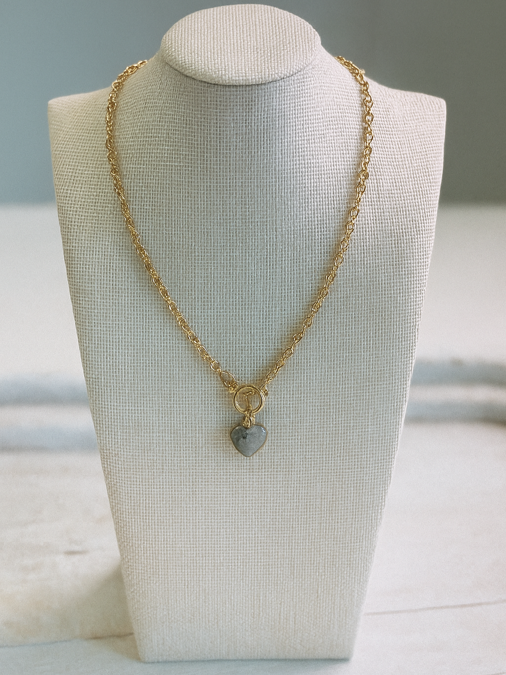 Gold necklace with small stone heart. It has a toggle closure.
