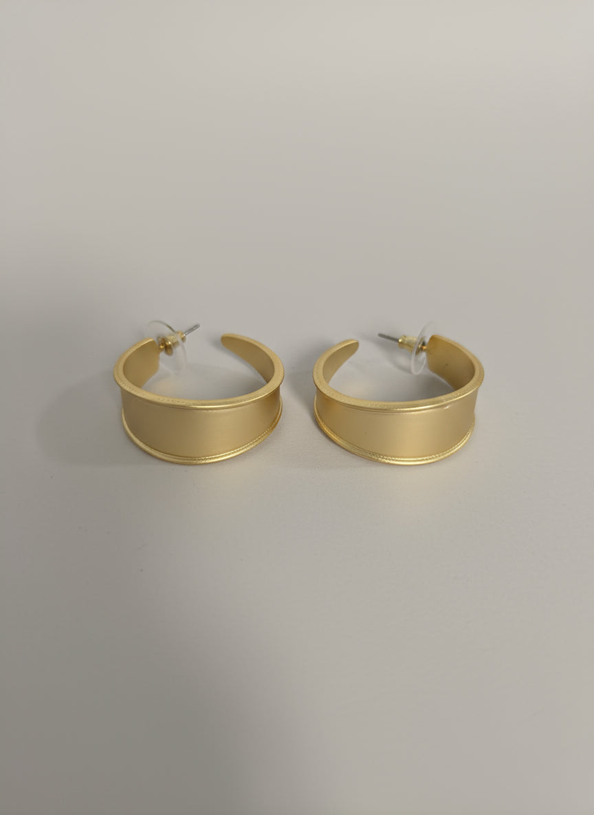 Gold hoop earrings displayed on a white surface with a decorative background