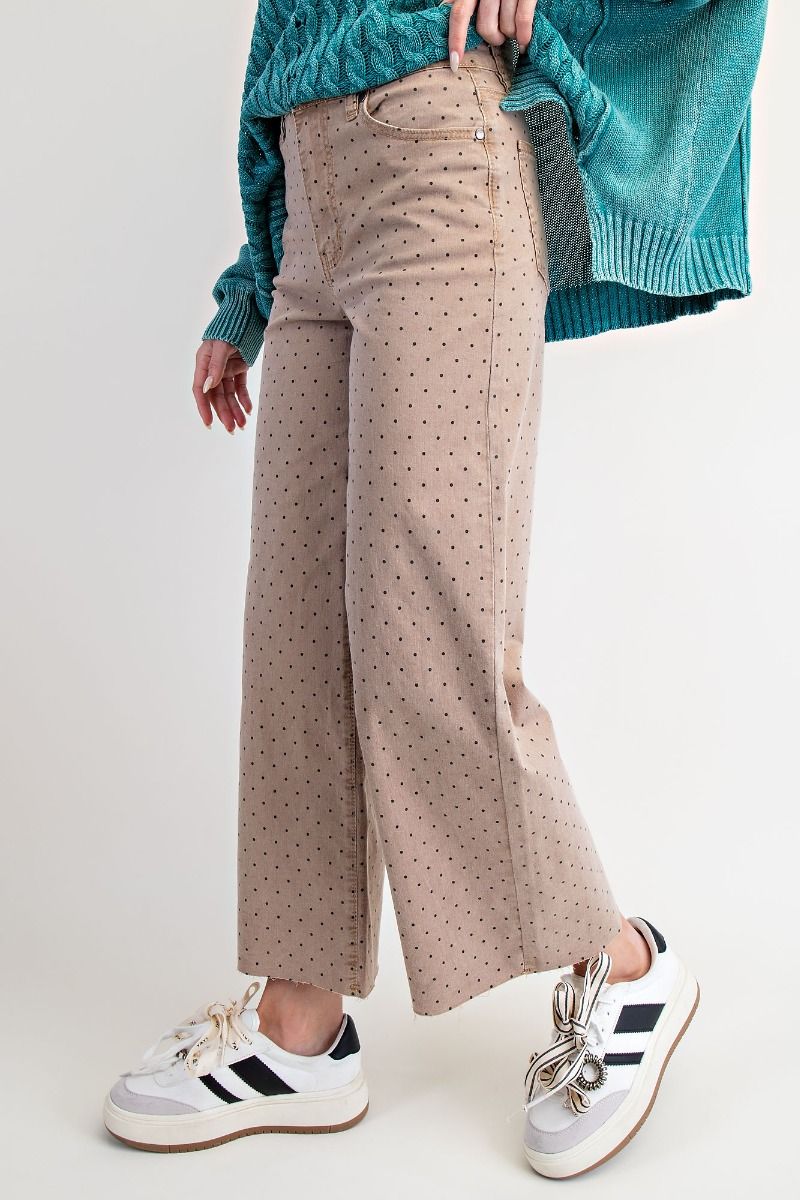 Person wearing beige polka dot pants with a teal sweater and white sneakers on a light background