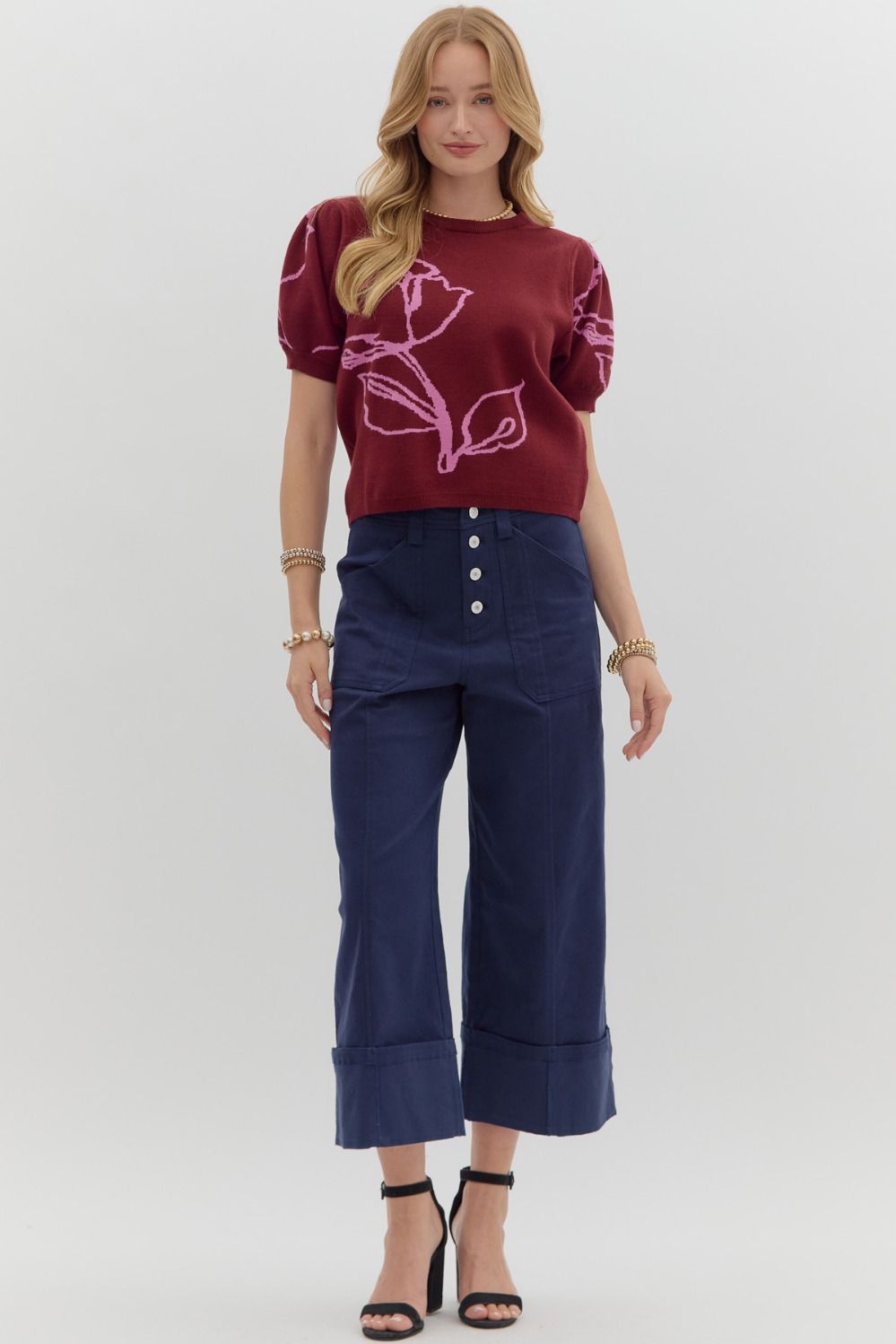 Woman wearing a maroon sweater with pink floral design and blue pants on a white background