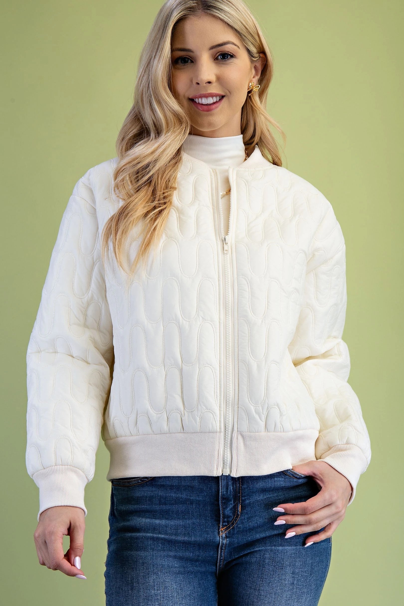 Woman wearing a cream quilted jacket against a green background