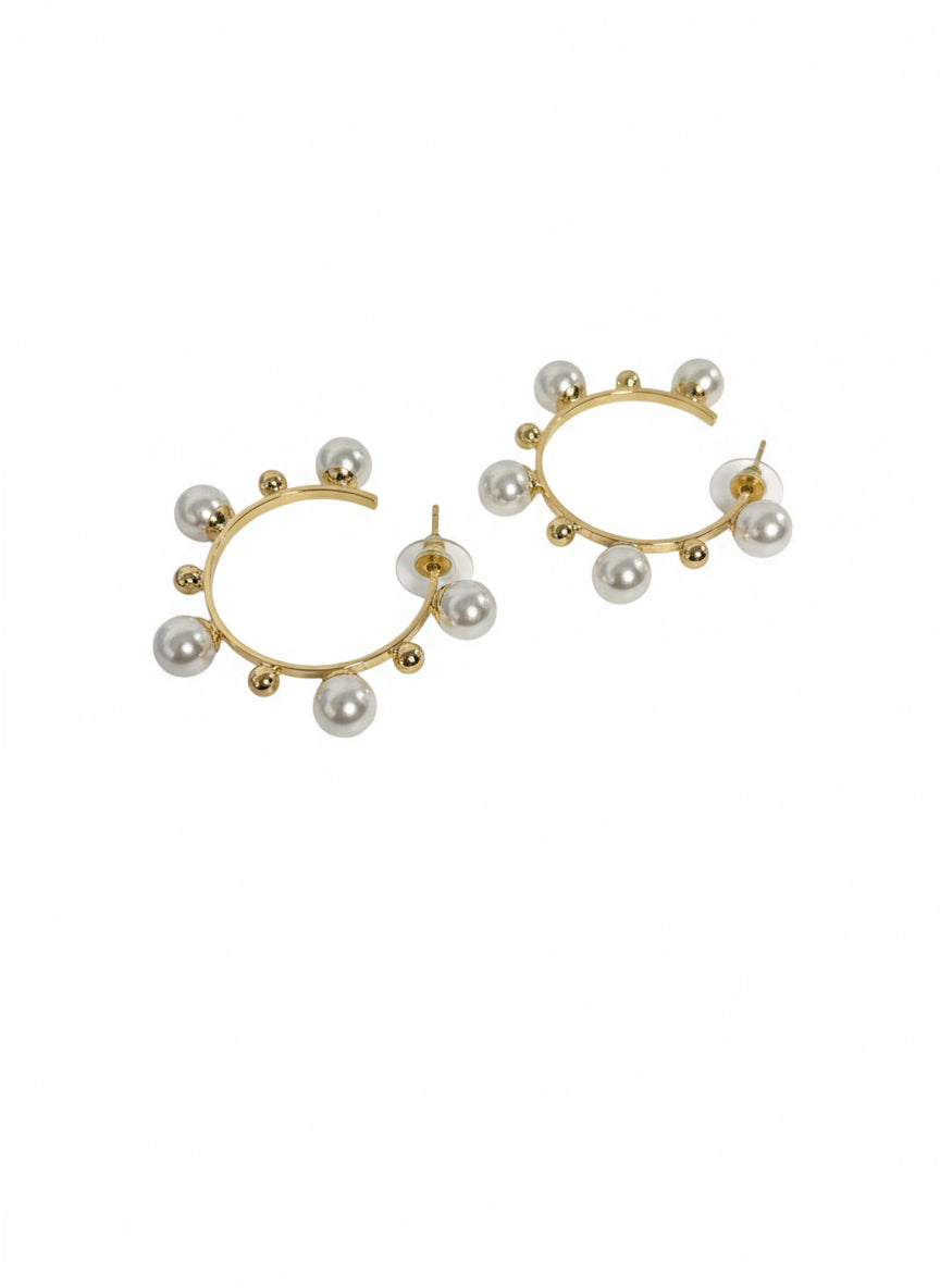 Gold hoop earrings with pearls on a decorative surface