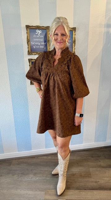 Brown lace-trimmed mini dress with leaf-print texture, ruffled neckline, and puff sleeves — styled with ivory cowboy boots for a chic fall look.