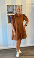 Woman wearing caramel brown tiered button-front dress with puff sleeves, ruffle details, and frayed hem, styled with sneakers and silver jewelry.