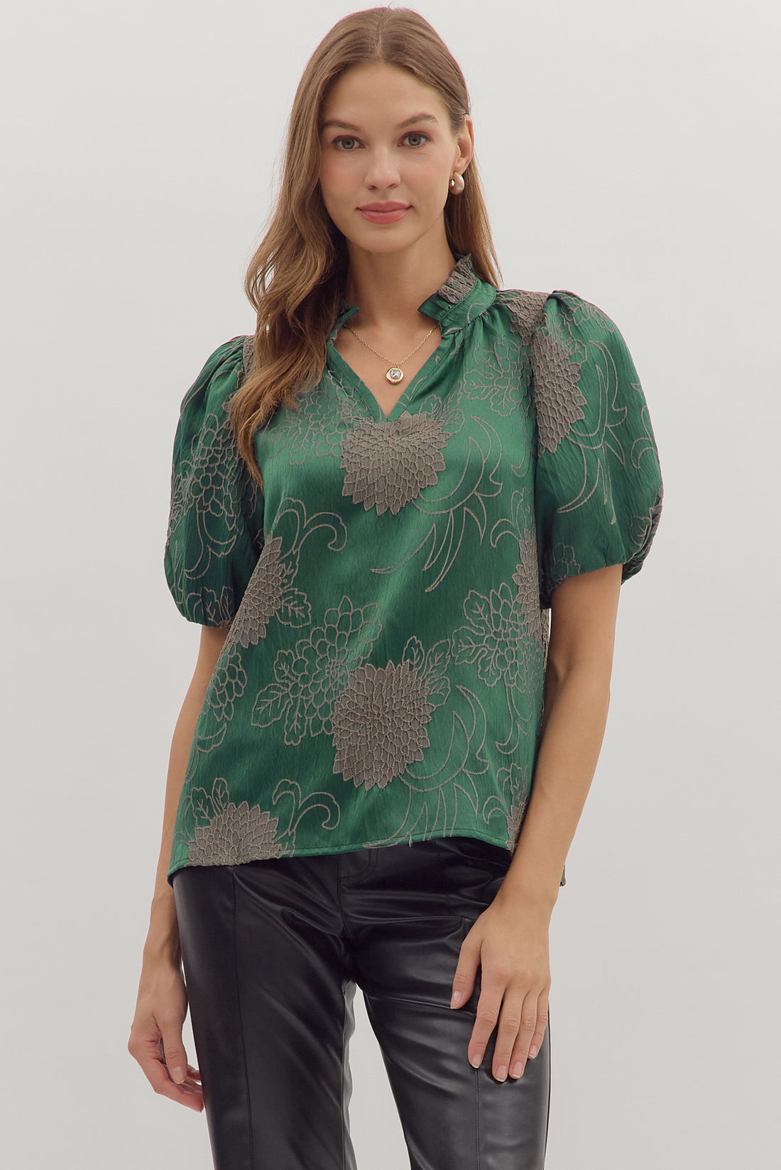 Model wearing the Emerald Reverie Top — a rich emerald green puff sleeve blouse with floral jacquard detailing and a notched neckline, styled with black leather pants.
