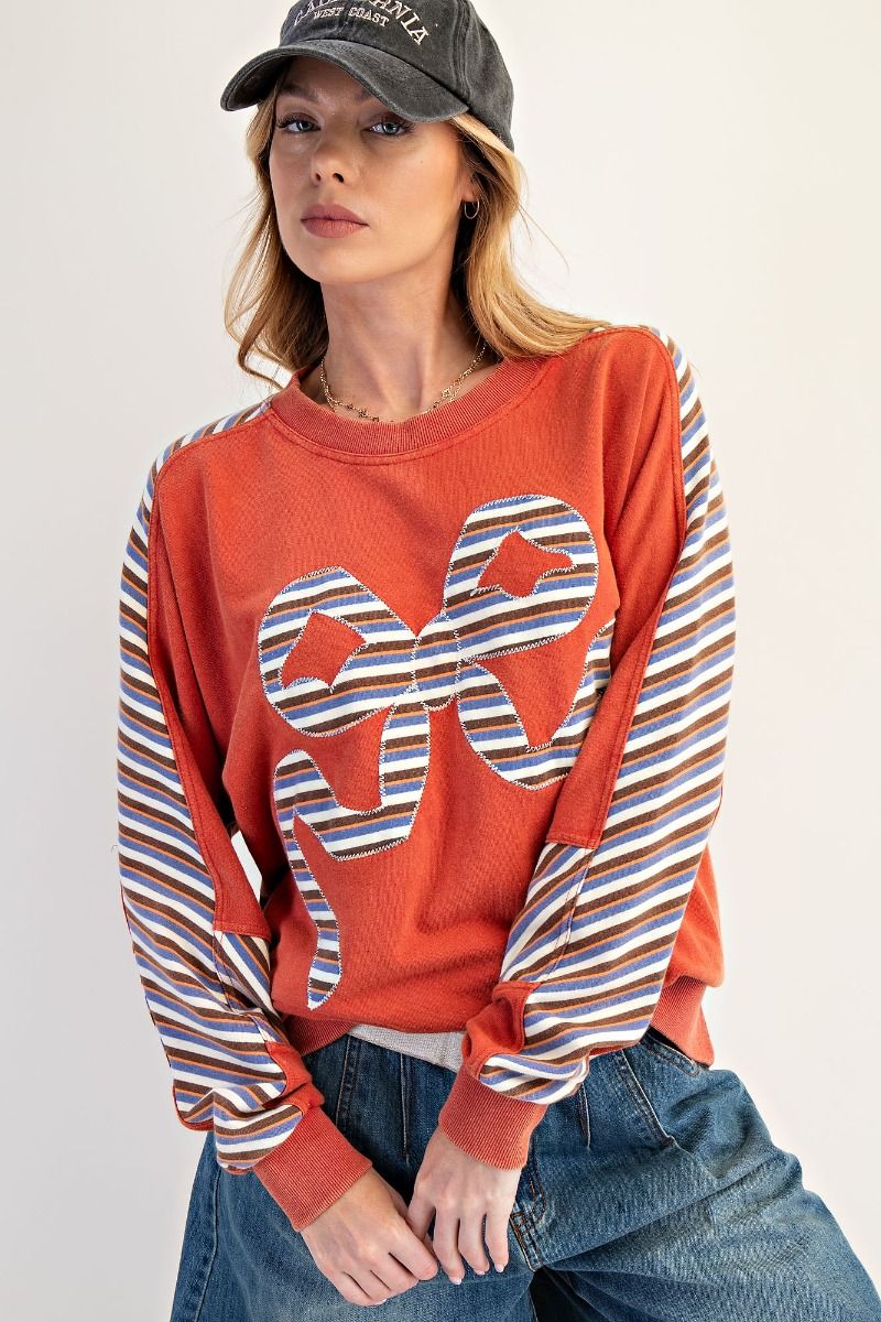 Woman wearing a red sweatshirt with striped sleeves and a cap on a plain background