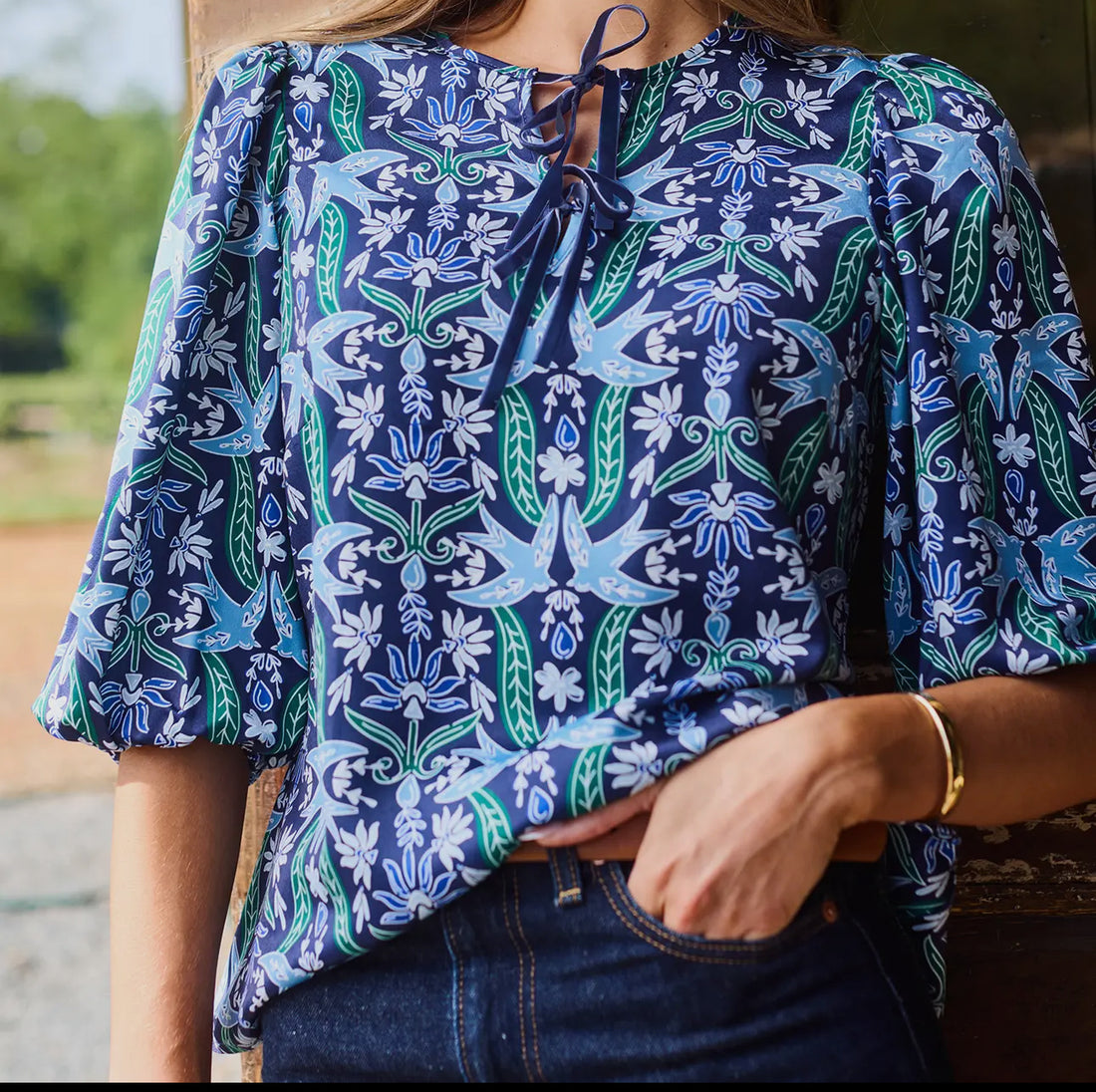 Navy blouse with blue and green floral and bird print, tie neckline, and relaxed half sleeves