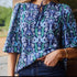 Navy blouse with blue and green floral and bird print, tie neckline, and relaxed half sleeves