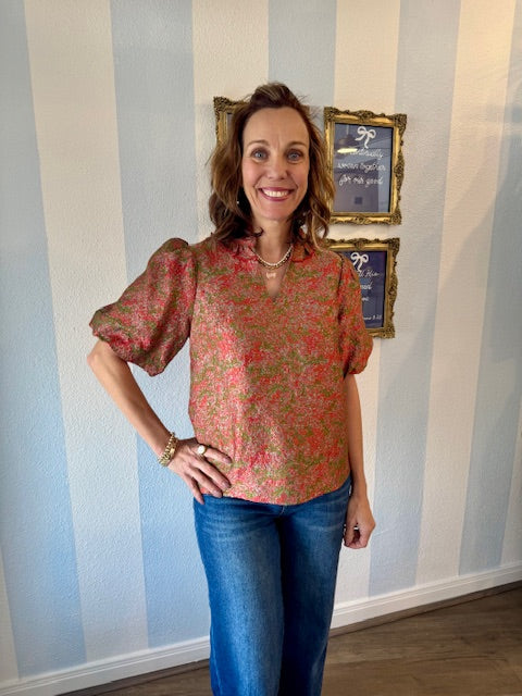 Woman wearing a floral blouse and blue jeans standing in front of a striped wall.