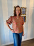 Woman wearing a floral blouse and blue jeans standing in front of a striped wall.