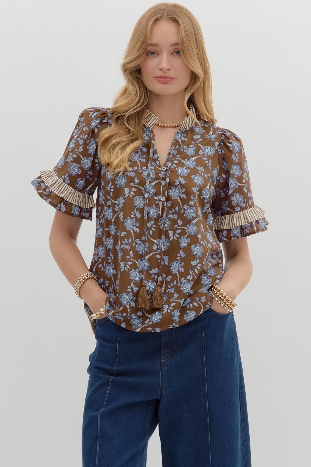 charming blouse features a rich brown background adorned with delicate blue floral prints, accented by pleated ruffle trim on the sleeves and neckline