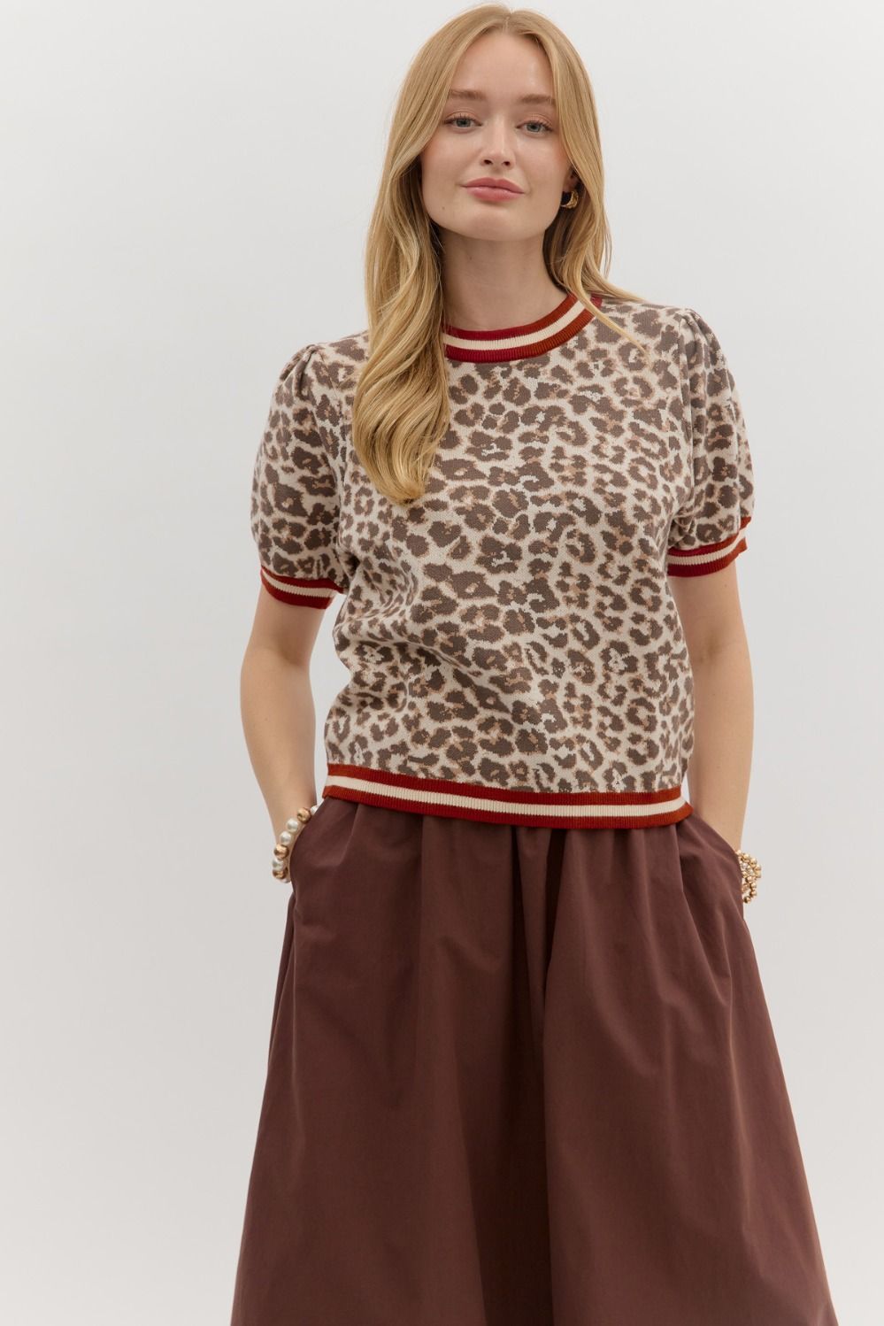 Featuring a classic leopard print in soft neutral tones, this top is elevated with bold red and ivory striped trim at the neckline, sleeves, and hem