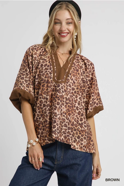 relaxed-fit blouse features a bold leopard print on a silky soft fabric, accented with rich brown ribbed trim at the V-notch neckline and sleeves
