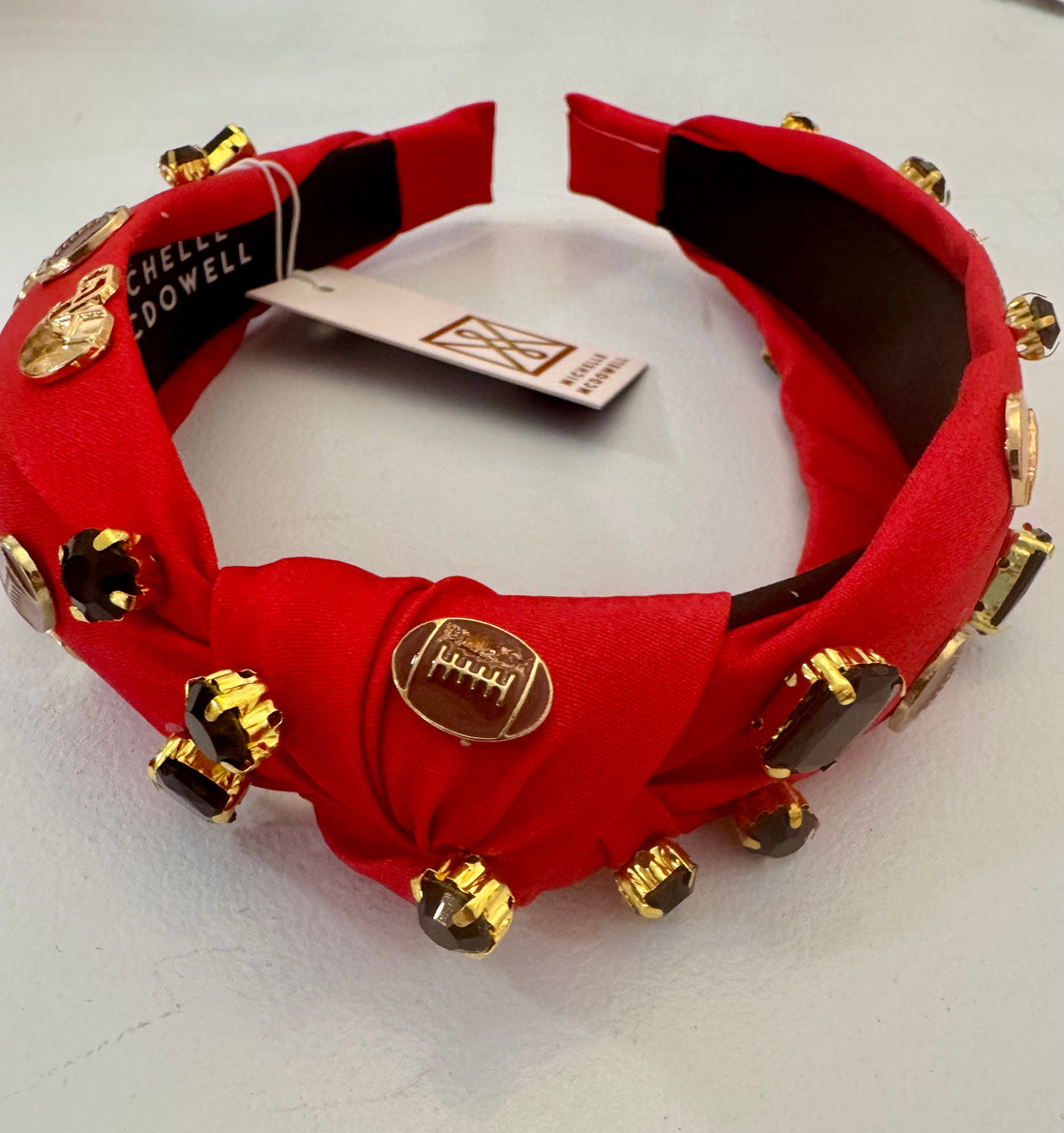 Knotted headband Featuring a bold red fabric base adorned with gold football helmets, mini football icons, and jewel-like gems