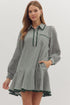 Woman wearing a green and white gingham long-sleeve mini dress with a collared neckline, ric-rac trim details, tiered hem, and side pockets, standing against a light background