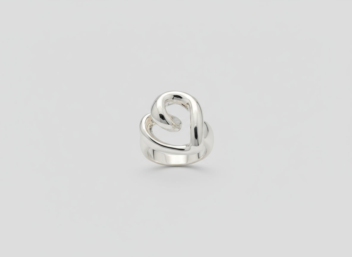 Hand wearing a silver heart-shaped ring on a wooden surface with a book in the background