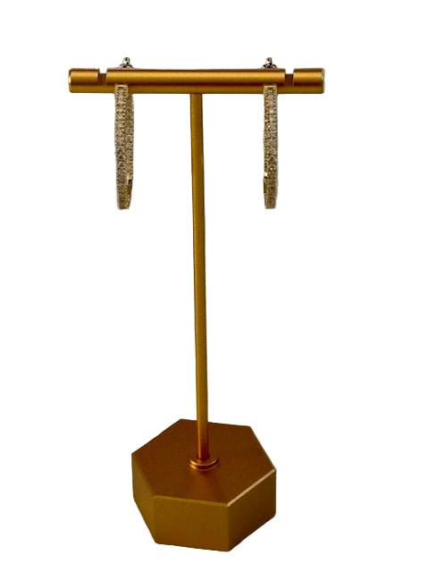 Gold earrings on a matching gold stand against a gray background