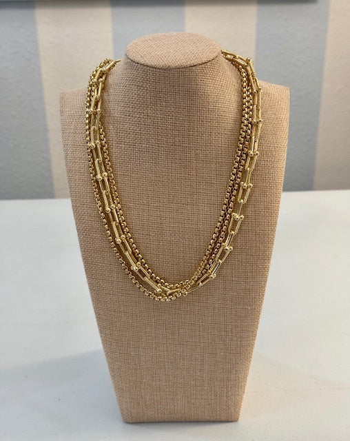 Gold necklace on a beige bust against a neutral background