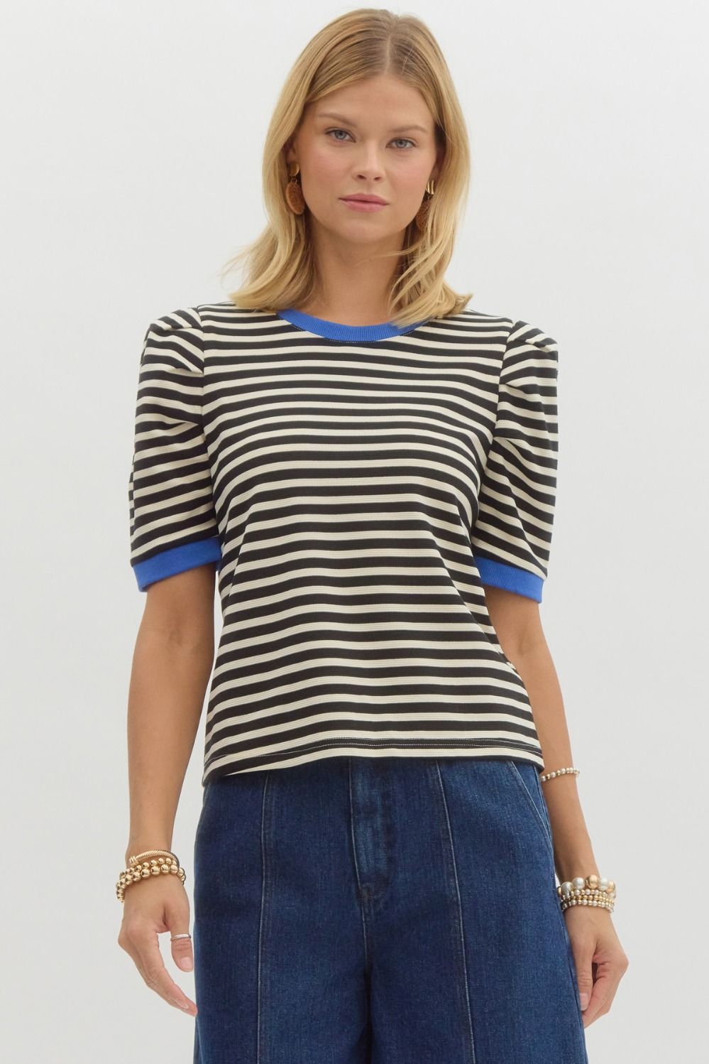 Woman wearing a black and white striped shirt with blue trim on a plain background