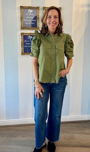 Woman wearing a green blouse and blue jeans standing in front of a striped wall.