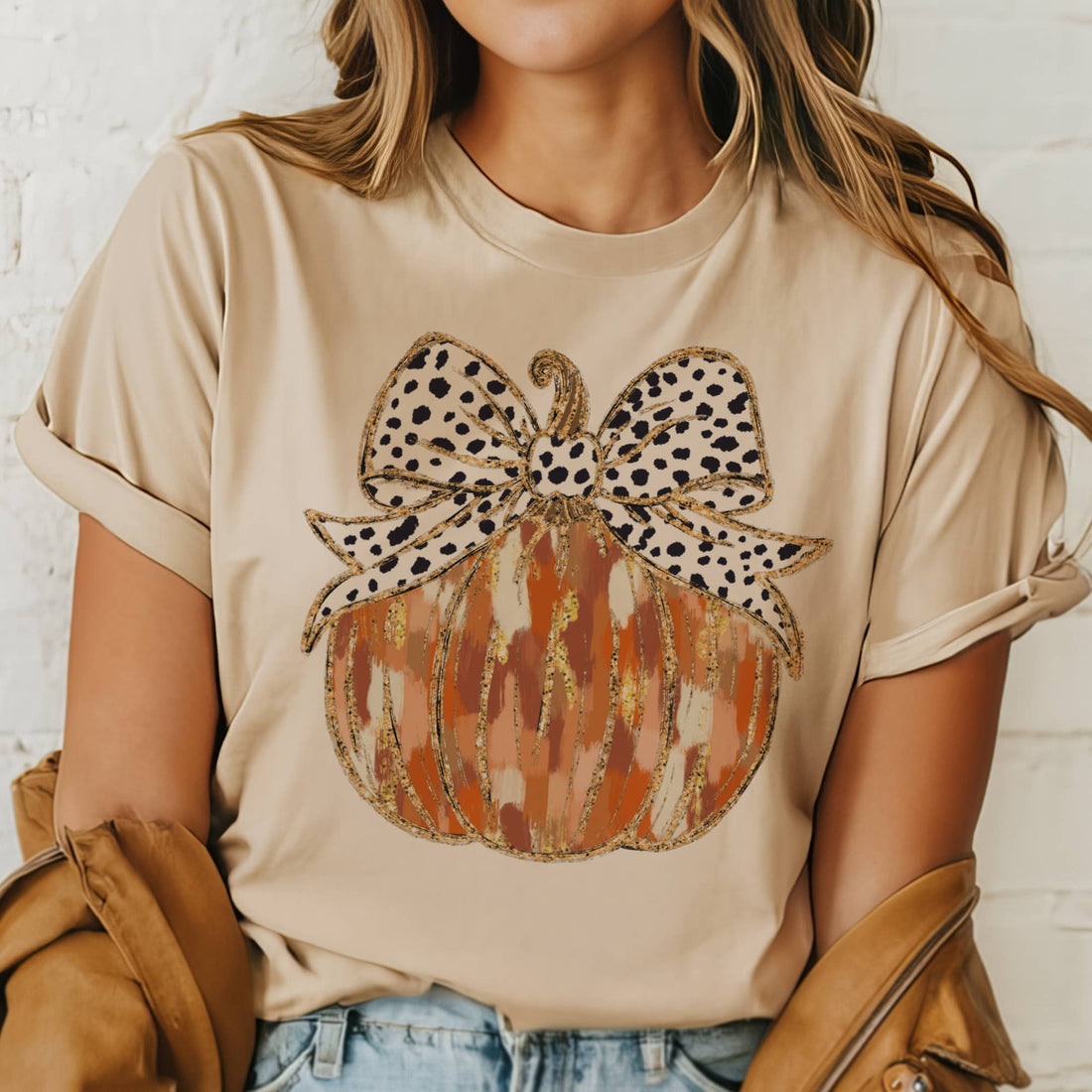 Person wearing a beige t-shirt with a pumpkin and bow design.