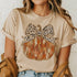 Person wearing a beige t-shirt with a pumpkin and bow design.