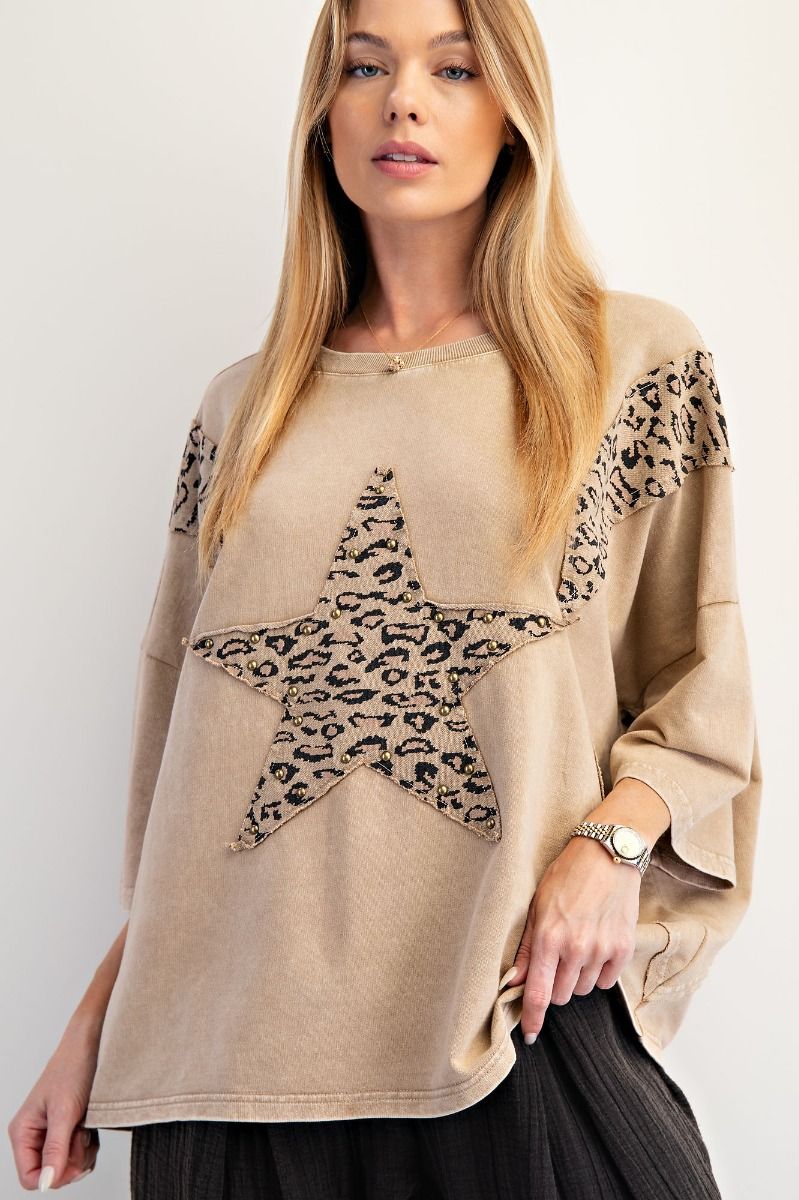 Woman wearing a beige sweater with a leopard print star design on a white background