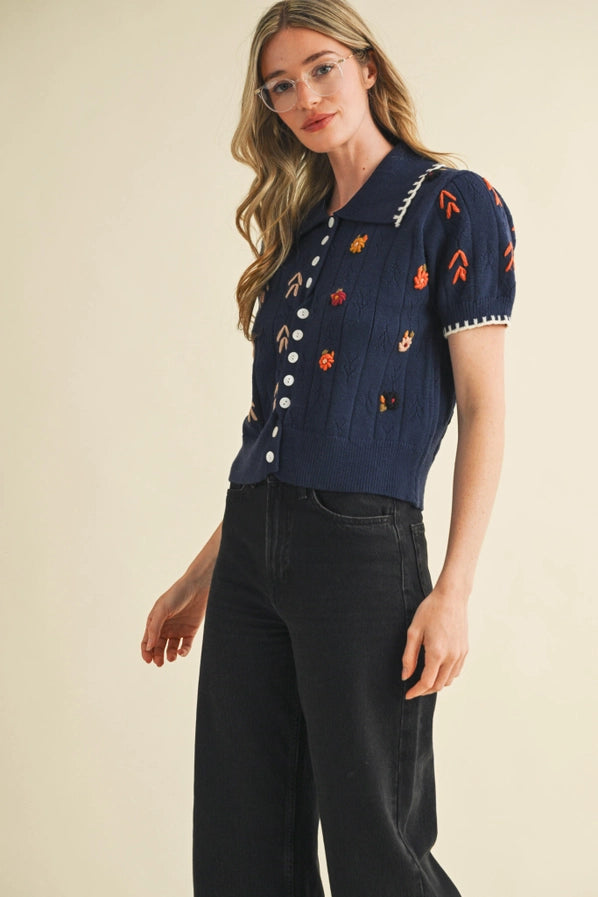 Woman wearing a navy blue embroidered shirt and black pants on a beige background