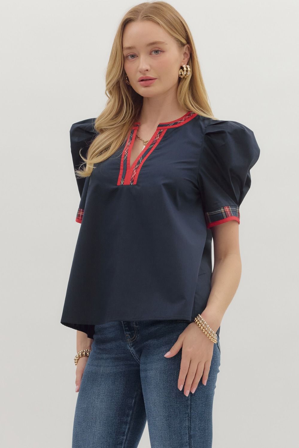 Woman wearing a navy blouse with red accents and blue jeans on a light gray background