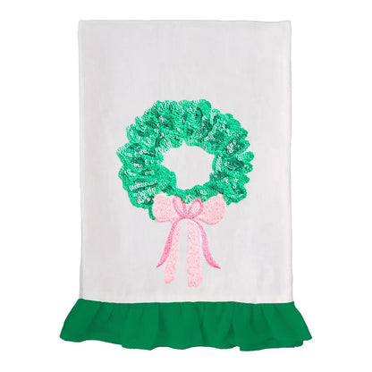 White tea towel with green sequin wreath and pink bow, finished with a green ruffle hem.