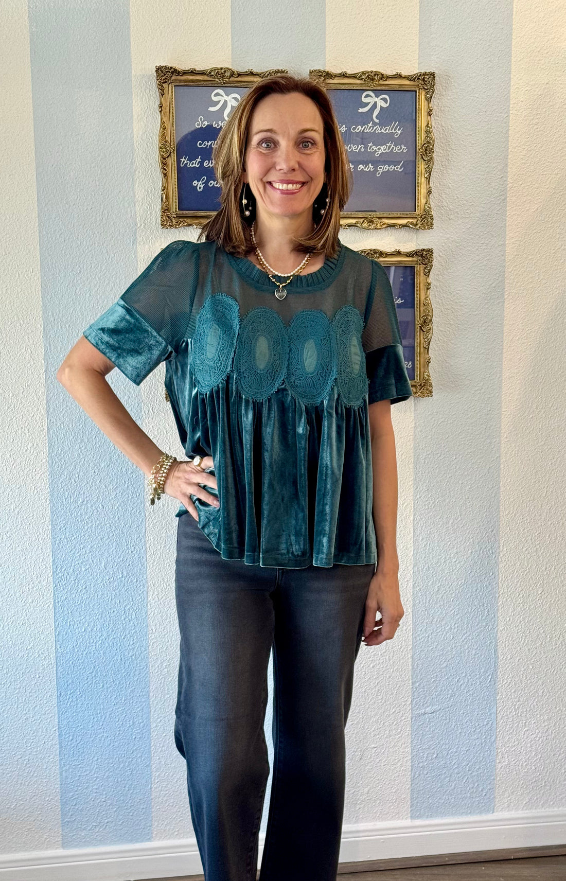 Woman wearing a teal blouse with a patterned design standing in front of a wall with framed pictures.
