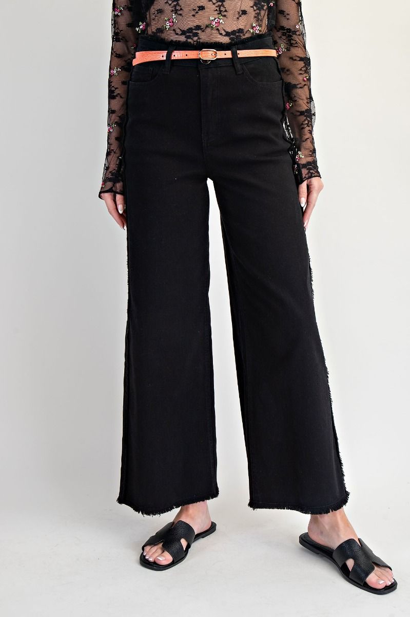 Person wearing black wide-leg jeans with a sheer top and sandals on a white background