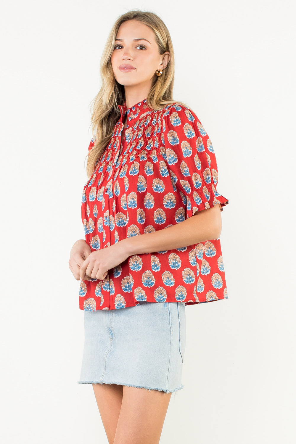 Woman wearing a red patterned blouse and light blue denim skirt on a white background