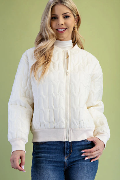 Woman wearing a cream quilted jacket against a green background